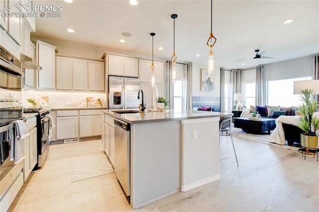 kitchen with hanging light fixtures, tasteful backsplash, light hardwood / wood-style flooring, a center island with sink, and appliances with stainless steel finishes