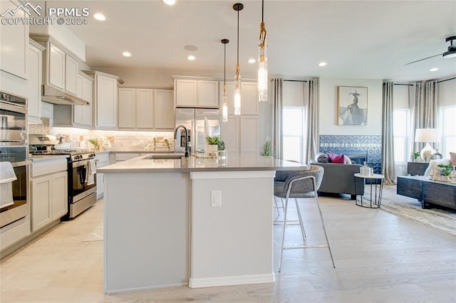 kitchen with hanging light fixtures, appliances with stainless steel finishes, a kitchen bar, and a kitchen island with sink