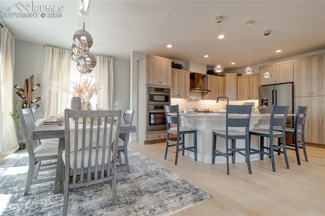 kitchen featuring light hardwood / wood-style flooring, hanging light fixtures, wall chimney range hood, and appliances with stainless steel finishes