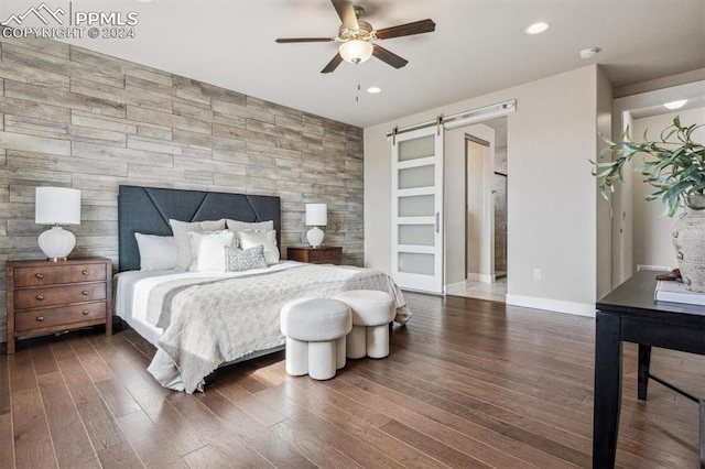 bedroom with dark hardwood / wood-style floors, a barn door, and ceiling fan