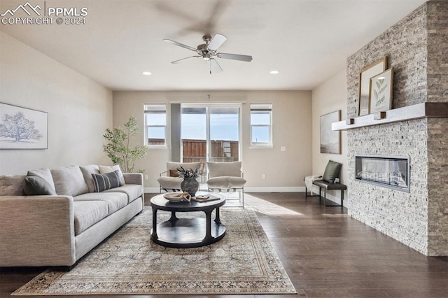 living room featuring dark hardwood / wood-style floors, ceiling fan, and a stone fireplace