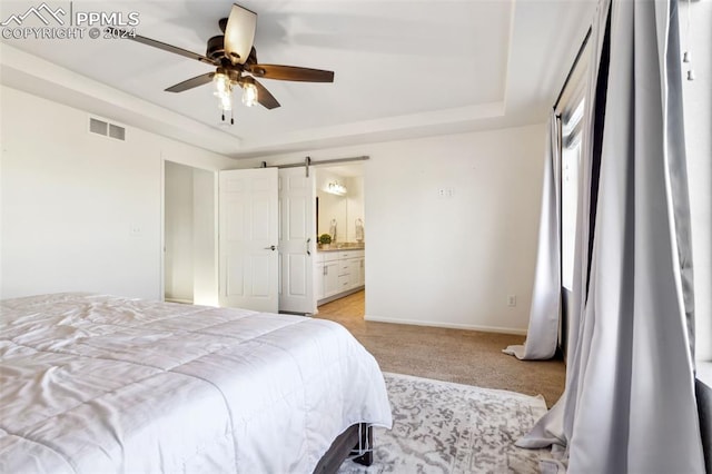 carpeted bedroom with a barn door, a tray ceiling, ceiling fan, and connected bathroom