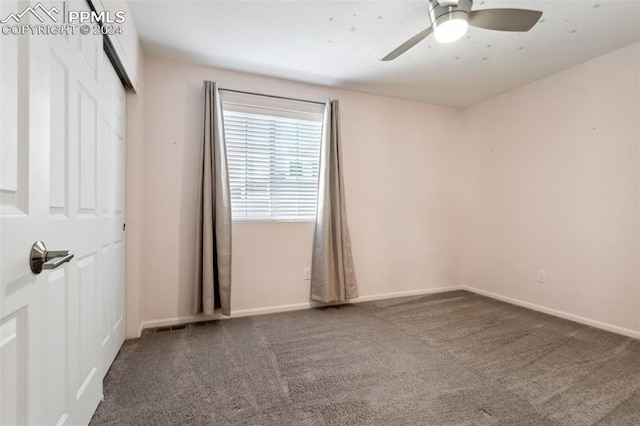 empty room featuring ceiling fan and dark carpet