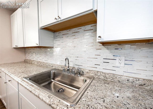 kitchen featuring white cabinets, decorative backsplash, light stone counters, and sink