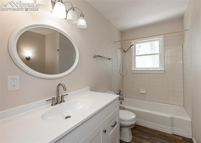 full bathroom with hardwood / wood-style floors, vanity, tiled shower / bath combo, and toilet