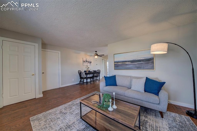 living room with a textured ceiling, ceiling fan, and dark wood-type flooring