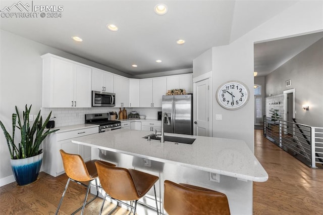 kitchen featuring dark wood-type flooring, an island with sink, appliances with stainless steel finishes, light stone counters, and white cabinetry