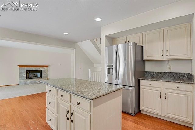 kitchen featuring stainless steel refrigerator with ice dispenser, a center island, light hardwood / wood-style flooring, and dark stone countertops