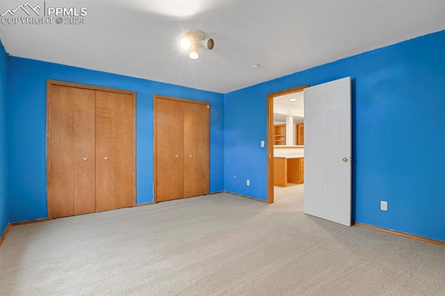 unfurnished bedroom featuring light colored carpet and multiple closets