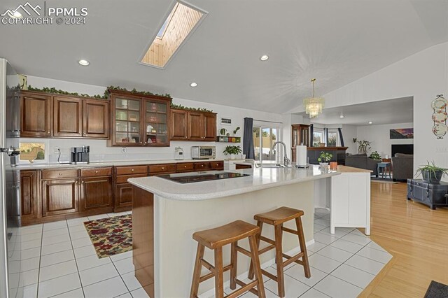 kitchen with sink, hanging light fixtures, black electric cooktop, a kitchen breakfast bar, and an island with sink