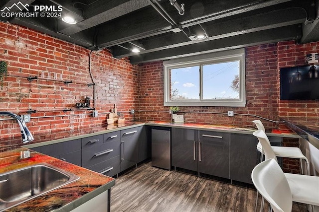 kitchen featuring refrigerator, sink, brick wall, and dark wood-type flooring