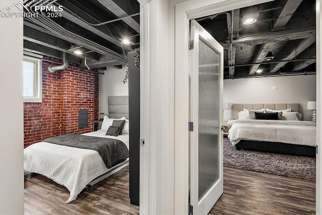 bedroom with dark wood-type flooring and brick wall