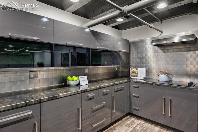 kitchen with decorative backsplash, black electric stovetop, and dark stone counters