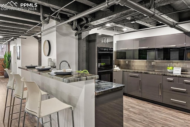 kitchen with a kitchen breakfast bar, light wood-type flooring, black double oven, and a kitchen island