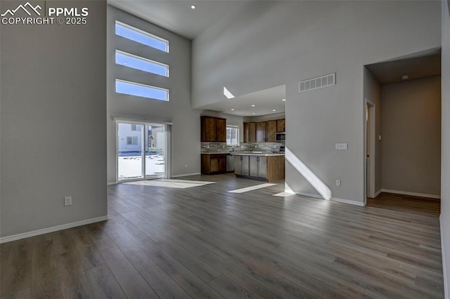 unfurnished living room featuring a towering ceiling, baseboards, visible vents, and wood finished floors