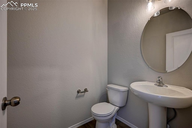 bathroom featuring baseboards, a textured wall, and toilet