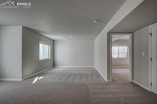 empty room featuring light carpet, a textured ceiling, and baseboards