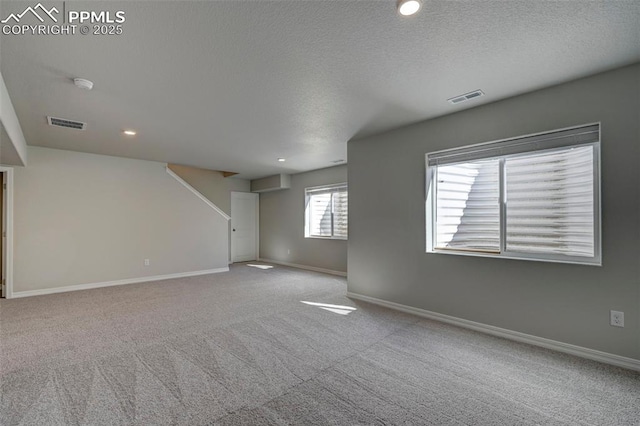 empty room with light colored carpet, visible vents, a textured ceiling, and baseboards