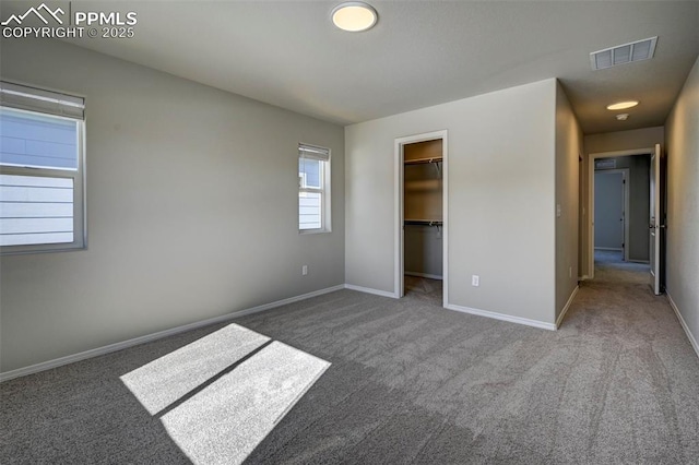 unfurnished bedroom with a spacious closet, carpet flooring, visible vents, and baseboards