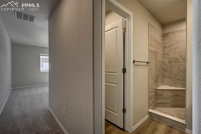 bathroom featuring wood finished floors, a tile shower, visible vents, and baseboards