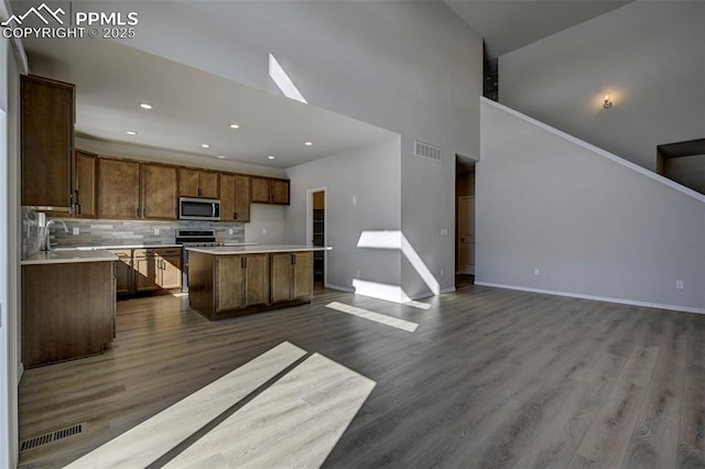 kitchen featuring brown cabinets, light countertops, appliances with stainless steel finishes, open floor plan, and a kitchen island