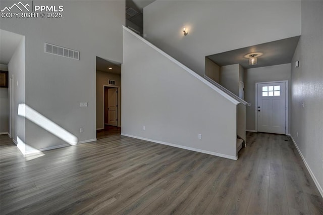 foyer entrance with wood finished floors, a towering ceiling, visible vents, stairs, and baseboards