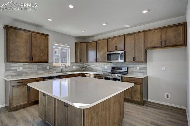 kitchen with appliances with stainless steel finishes, a center island, light countertops, light wood-type flooring, and a sink