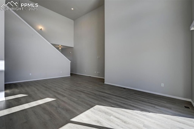 unfurnished living room featuring dark wood-style flooring, a towering ceiling, and baseboards