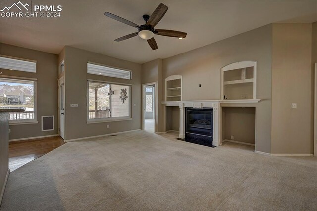 unfurnished living room featuring light carpet, built in shelves, and ceiling fan