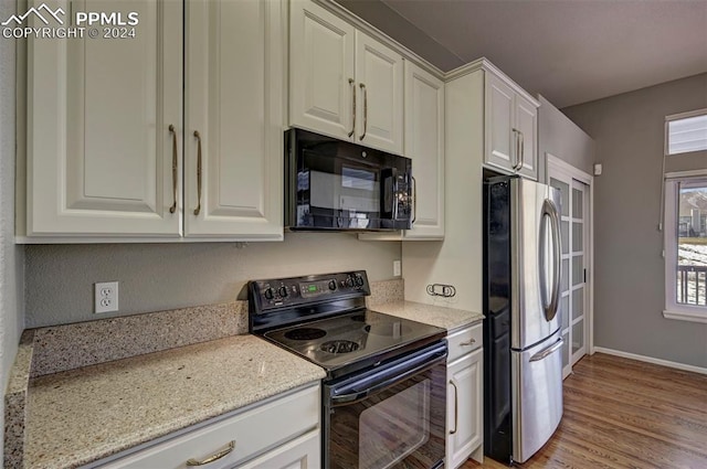 kitchen with black appliances, white cabinetry, light stone countertops, and light hardwood / wood-style flooring