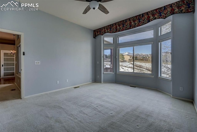 carpeted empty room featuring ceiling fan with notable chandelier