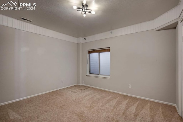 carpeted empty room featuring a chandelier and a textured ceiling