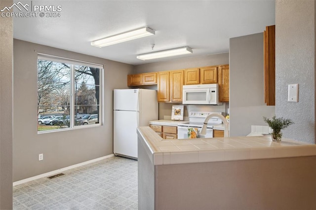 kitchen with kitchen peninsula, white appliances, and tile counters