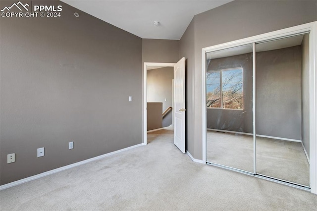 unfurnished bedroom with a closet, light colored carpet, and lofted ceiling