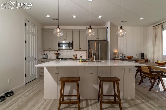 kitchen featuring gray cabinets, light wood-type flooring, a kitchen island with sink, and appliances with stainless steel finishes