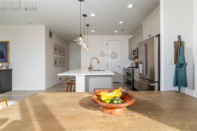 kitchen featuring high end appliances, sink, gray cabinets, an island with sink, and a breakfast bar area