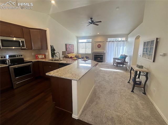 kitchen featuring sink, dark colored carpet, kitchen peninsula, lofted ceiling, and appliances with stainless steel finishes