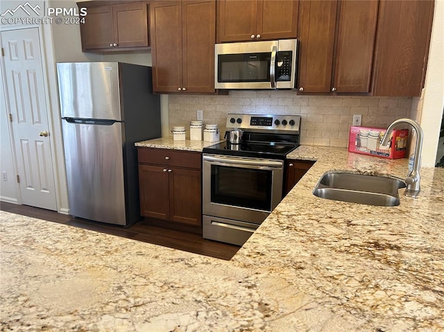 kitchen with light stone countertops, sink, dark hardwood / wood-style floors, decorative backsplash, and appliances with stainless steel finishes