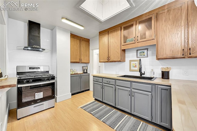 kitchen featuring gray cabinetry, sink, wall chimney exhaust hood, stainless steel gas range oven, and light wood-type flooring