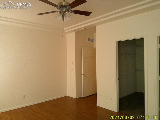 unfurnished bedroom with ceiling fan, a walk in closet, dark wood-type flooring, and a closet