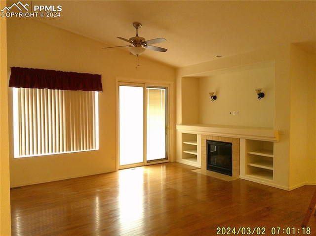 unfurnished living room featuring built in shelves, ceiling fan, a tiled fireplace, and hardwood / wood-style flooring