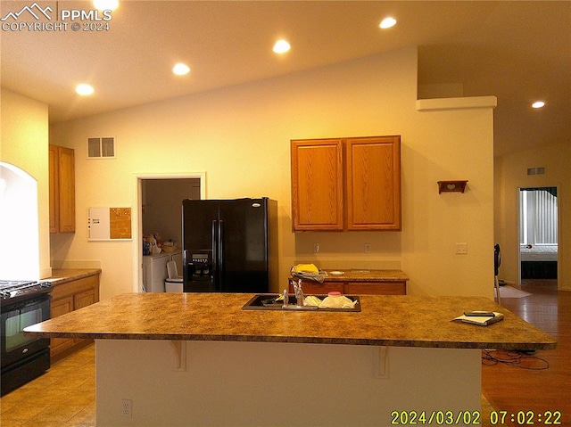 kitchen with a kitchen breakfast bar, vaulted ceiling, sink, black appliances, and an island with sink