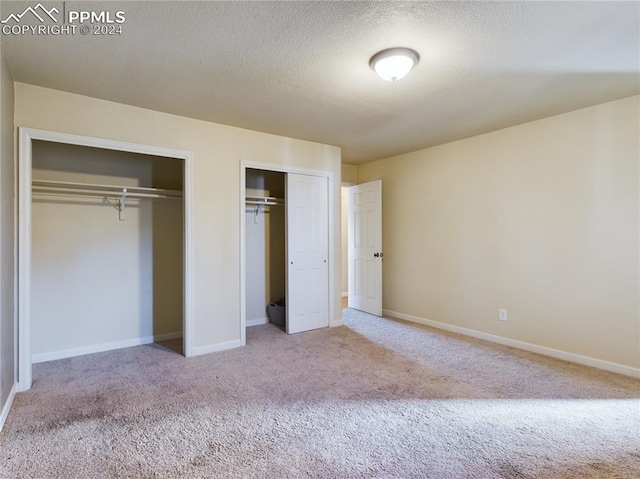 unfurnished bedroom featuring a textured ceiling, two closets, and light colored carpet