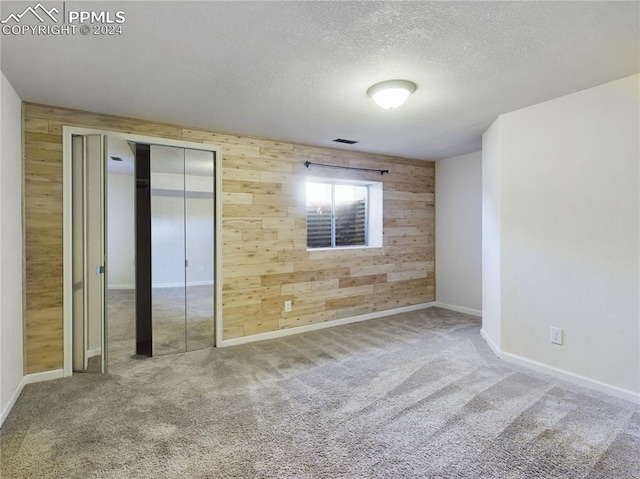 unfurnished bedroom with carpet, a textured ceiling, a closet, and wooden walls