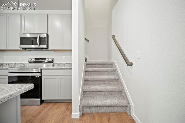 kitchen with gray cabinets, light stone countertops, light hardwood / wood-style floors, and appliances with stainless steel finishes