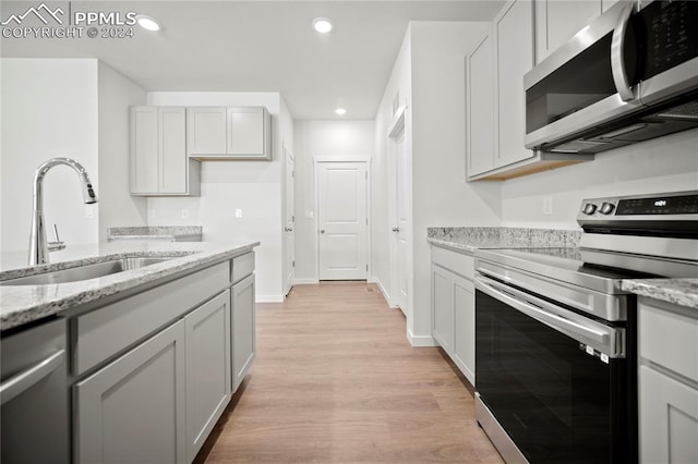 kitchen with white cabinetry, sink, stainless steel appliances, light stone counters, and light hardwood / wood-style flooring