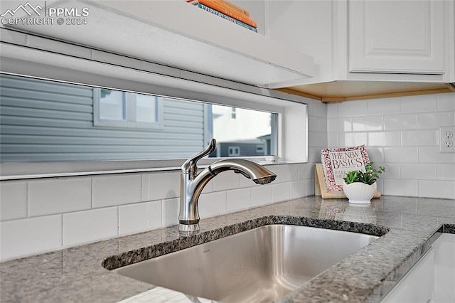 interior details featuring white cabinets, decorative backsplash, light stone countertops, and sink