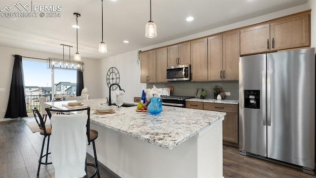 kitchen with decorative light fixtures, dark wood-type flooring, stainless steel appliances, and an island with sink