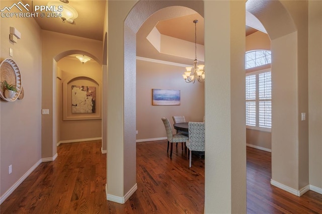 corridor featuring a tray ceiling, an inviting chandelier, and dark wood-type flooring