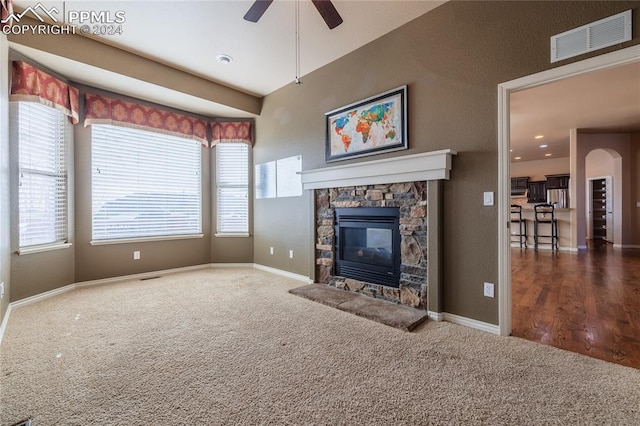 unfurnished living room featuring ceiling fan, dark carpet, a healthy amount of sunlight, and a fireplace